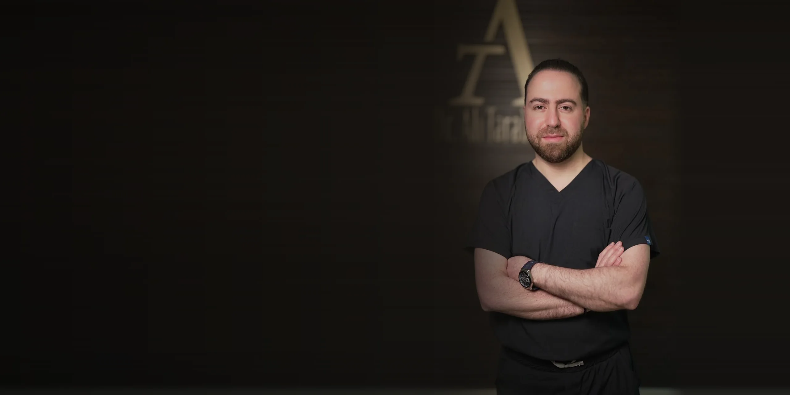 Dr. Ali Tarabaih in his clinic, in front of the clinic logo